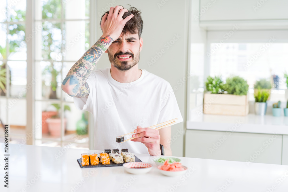 Young man eating asian sushi from home delivery stressed with hand on head, shocked with shame and surprise face, angry and frustrated. Fear and upset for mistake. Young man eating asian sushi from home delivery stressed with hand on head, shocked with shame and surprise face, angry and frustrated. Fear and upset for mistake.