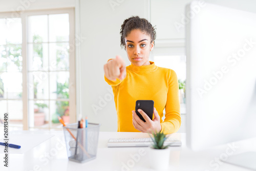 Young african american girl working using computer and smartphone pointing with finger to the camera and to you, hand sign, positive and confident gesture from the front