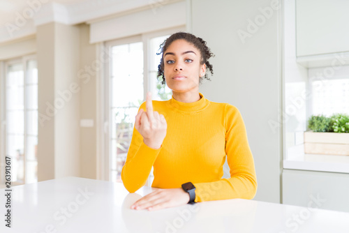 Beautiful african american woman with afro hair wearing a casual yellow sweater Showing middle finger, impolite and rude fuck off expression