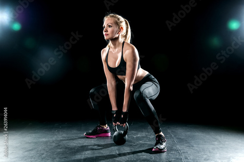 The girl performs squats with a weight in the spotlight.