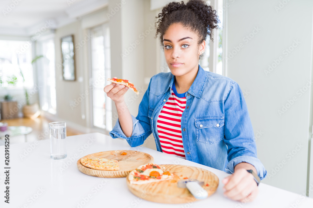 Young african american woman eating two homemade cheese pizzas with a confident expression on smart face thinking serious Young african american woman eating two homemade cheese pizzas with a confident expression on smart face thinking serious