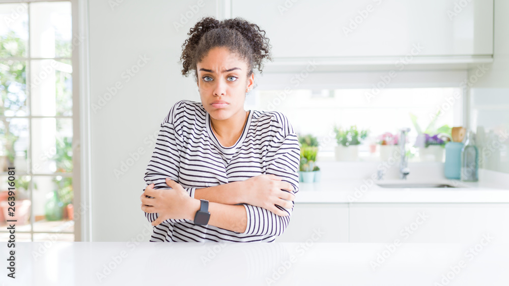 Beautiful african american woman with afro hair wearing casual striped sweater shaking and freezing for winter cold with sad and shock expression on face Beautiful african american woman with afro hair wearing casual striped sweater shaking and freezing for winter cold with sad and shock expression on face