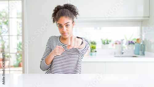 Beautiful african american woman with afro hair wearing casual striped sweater Punching fist to fight, aggressive and angry attack, threat and violence