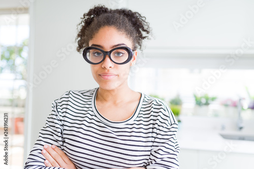 Beautiful young african american woman with afro hair wearing glasses Relaxed with serious expression on face. Simple and natural with crossed arms © Krakenimages.com