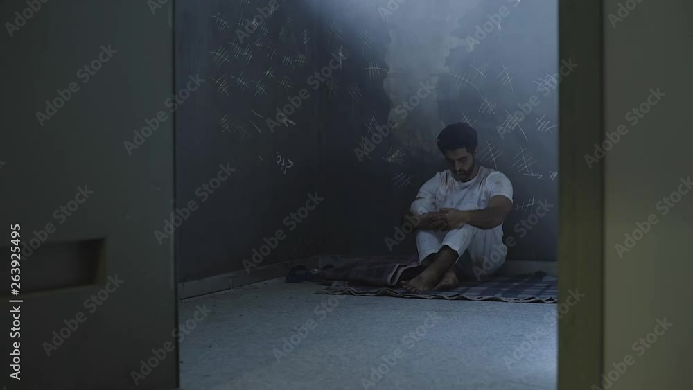 A sad oppressed young man sitting in prison dark room A sad oppressed young man sitting in prison dark room