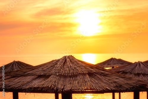 Straw beach umbrellas on the golden sunset background, summer travel and relax landscape