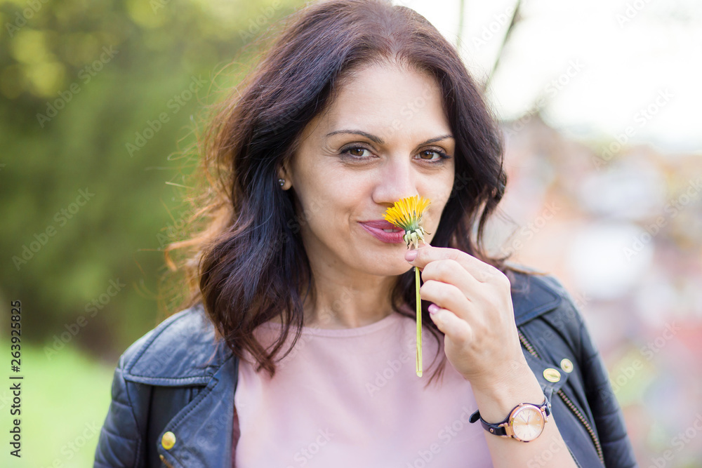 Beautiful middle-age woman in black leather jacket smelling daisy flower. Beautiful middle-age woman in black leather jacket smelling daisy flower.