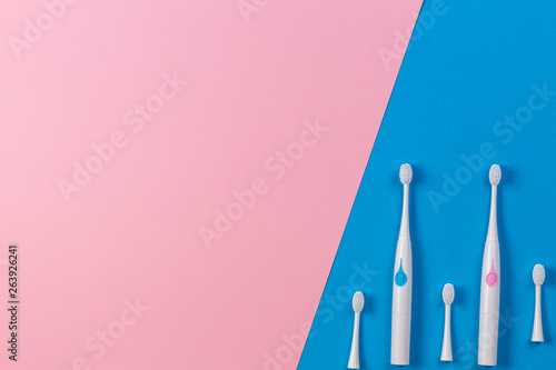Two electric toothbrushes with three brush heads on blue and pink background. Top view