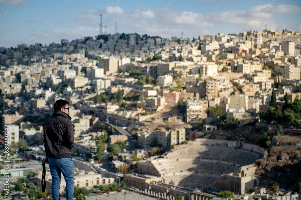 Young Asian man tourist enjoy looking at the view of Amman city from Citadel viewpoint, a historical site at the center of downtown Amman, Jordan. Travel Middle East concept.