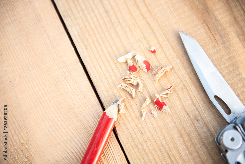 Background with tools. Pencil red sharpened with a folding knife lies on a wooden background Background with tools. Pencil red sharpened with a folding knife lies on a wooden background