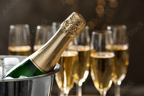 Bottle of champagne in bucket with ice and glasses on blurred background, closeup. Space for text photo