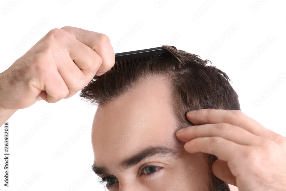 Fototapeta premium Young man with comb on white background, closeup. Hair loss problem