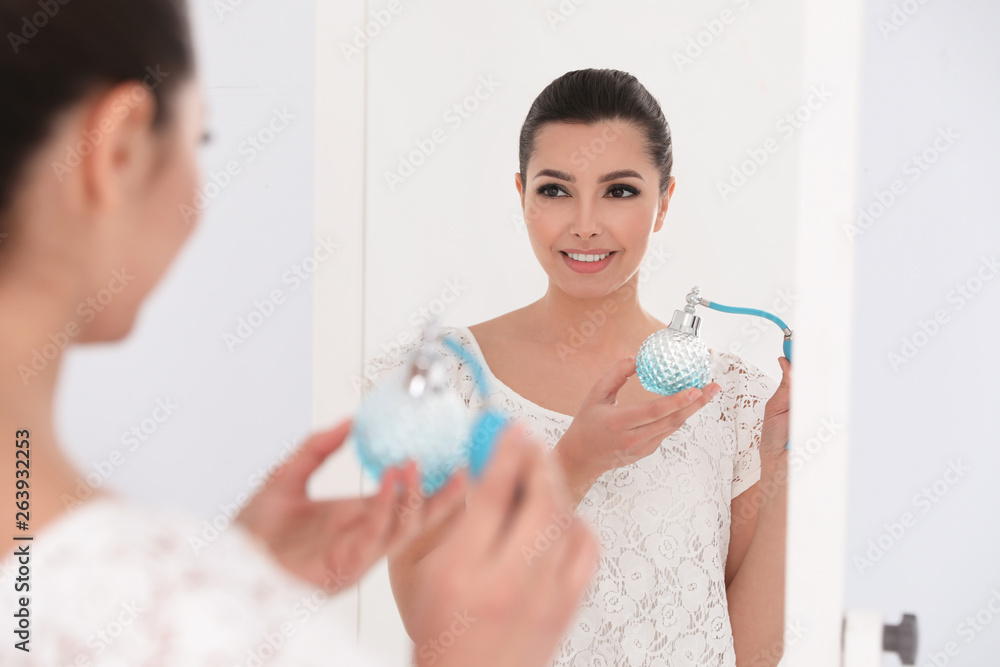 Young woman with bottle of perfume near mirror indoors Young woman with bottle of perfume near mirror indoors