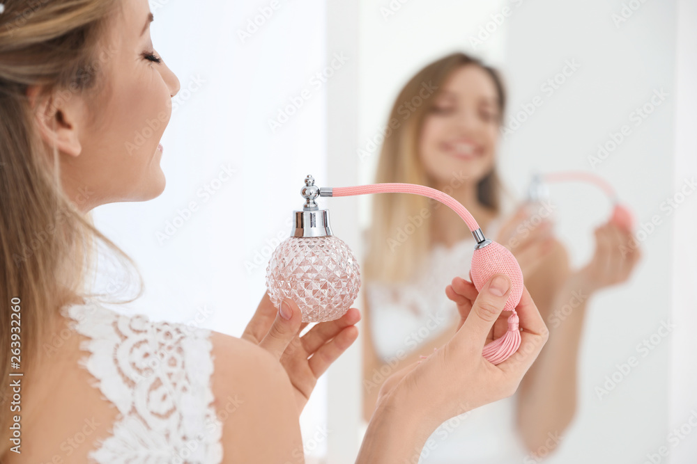 Beautiful young bride with bottle of perfume near mirror indoors - obrazy, fototapety, plakaty 