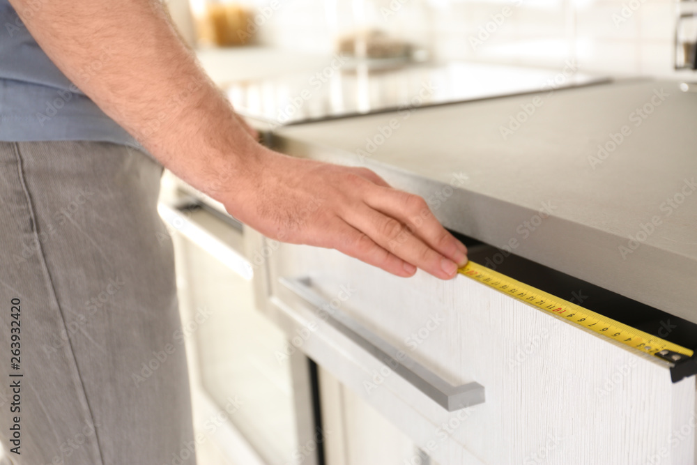 Obraz premium Man measuring kitchen furniture indoors, closeup. Construction tool