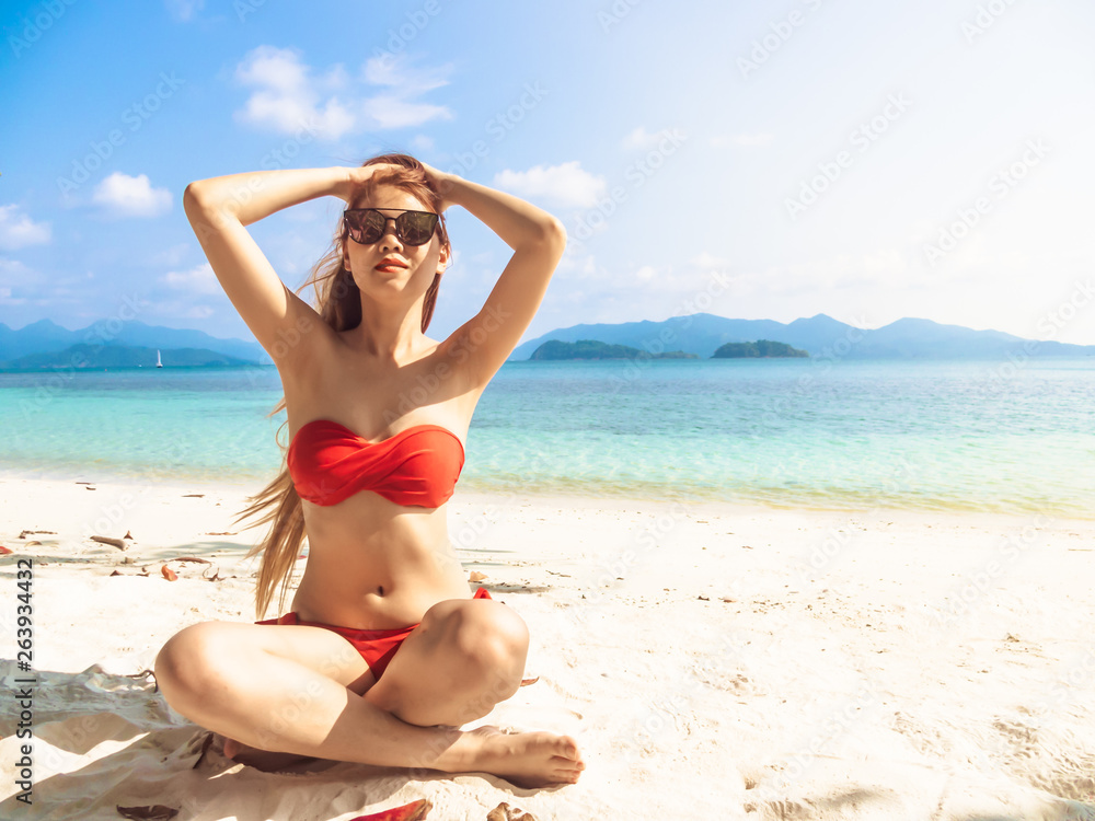 sun protection and skin care concept from young woman fashion model in red bikini sit on beach enjoying the summer on sunny days, image soft focus lens flare sunlight, have copy space for advertising.
