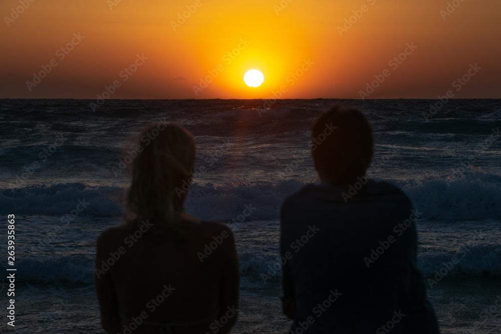 Two girls sit on the beach and watch the sunset
