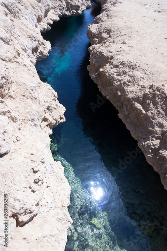 The reflection of the sunblock in a small creek of a blue-blue color flowing between light yellow gray brown brown stones. Vertical photo