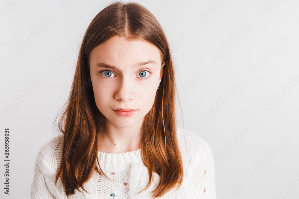 Emotional teen girl in a white knitted sweater on a light gray background.Space for text. Emotional teen girl in a white knitted sweater on a light gray background.Space for text.