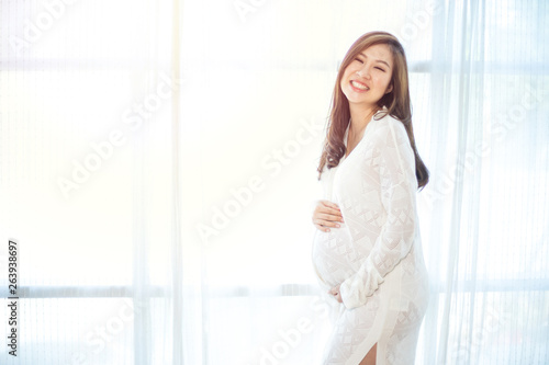 Free Download Young Asian beautiful pregnant woman standing near window - GFXLoad
