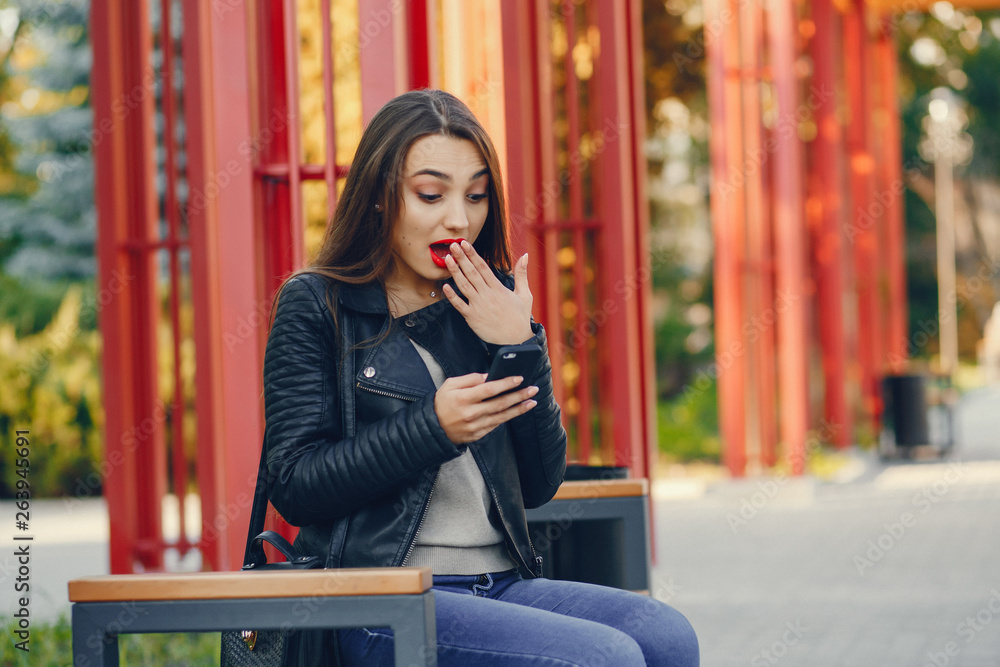Fototapeta premium young and pretty girl sitting in a summer city with phone