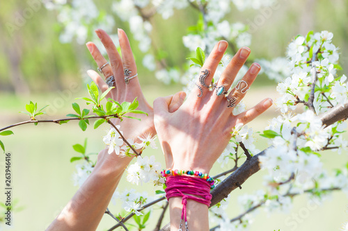 young woman hands with lot of rings and bracelets in bird symbol gesture in front cherry blossom closeup