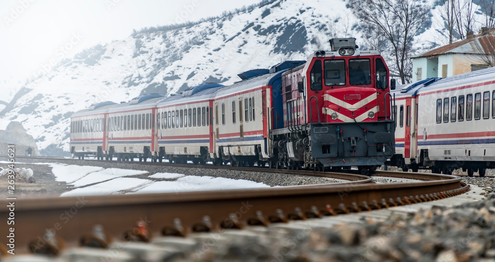 Fototapeta premium Train at snow covered railway line in snowy valley between the mountains.