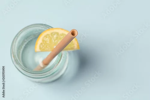 Obraz Słoma bambusowa w szklance wody cytrynowej na niebieskim tle, słomki bambusowe wielokrotnego użytku jako alternatywa dla jednorazowych plastikowych słomek, koncepcja zdrowego i zrównoważonego stylu życia