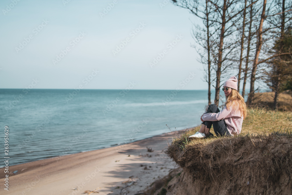 Young adult woman in pink hat sitting alone on the bluffs, looking of sea, freedom concept, peaceful atmosphere, meditation, copy space, Latvia, Jurkalne Young adult woman in pink hat sitting alone on the bluffs, looking of sea, freedom concept, peaceful atmosphere, meditation, copy space, Latvia, Jurkalne