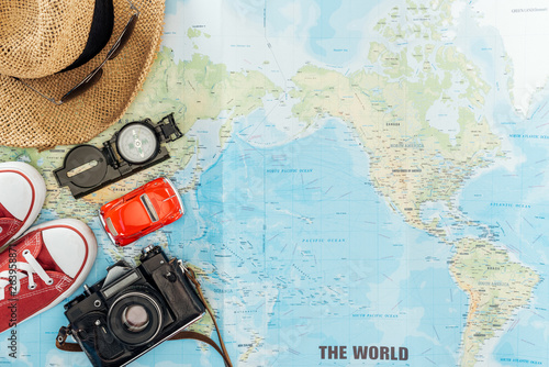 Top view of gumshoes, straw hat, sunglasses, film camera, toy car and compass on world map photo