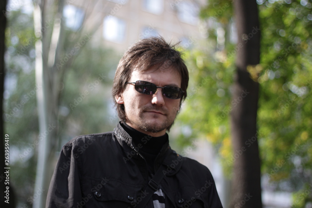 a man in a black jacket and sunglasses in the park a man in a black jacket and sunglasses in the park