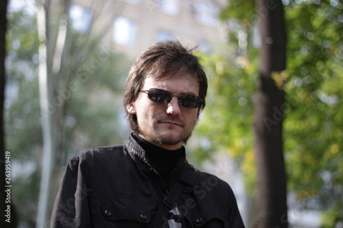 a man in a black jacket and sunglasses in the park