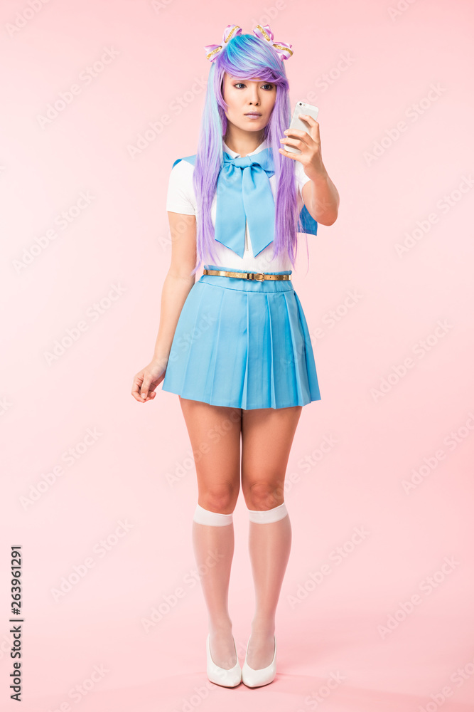 Full length view of asian anime girl holding smartphone on pink Full length view of asian anime girl holding smartphone on pink