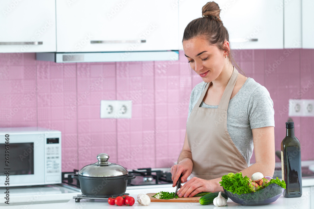 Attractive young cooking woman in apron chopping vegetables for salad for dinner at kitchen at home. Clean healthy food and proper nutrition. Diet
