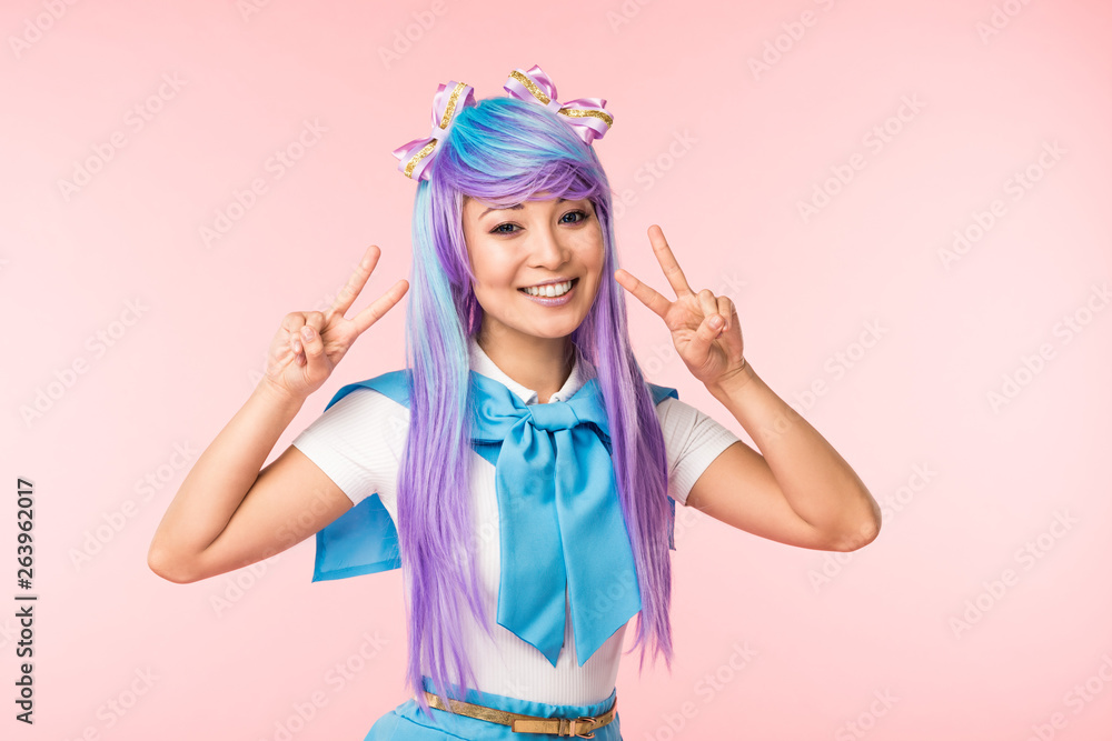 Joyful asian anime girl in purple wig showing peace signs isolated on pink