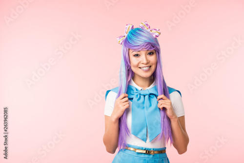Laughing asian anime girl touching hair isolated on pink