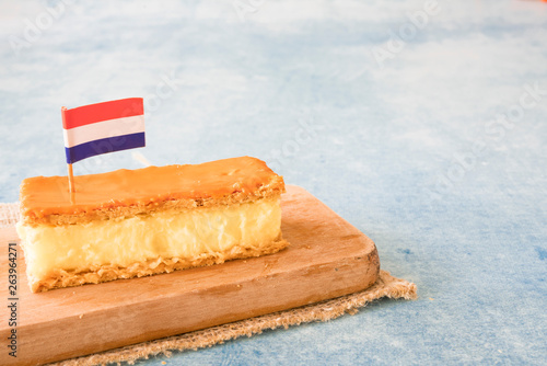 Orange tompouce, traditional Dutch treat with pudding and frosting on national holiday Kings Day (April 27th), in The Netherlands. Blue background, space for text
