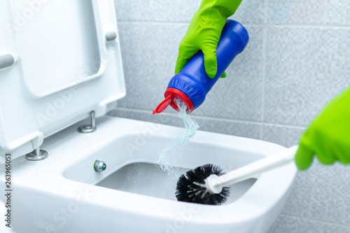 Fototapeta Naklejka Na Ścianę i Meble -  Housemaid in rubber gloves washing and disinfecting toilet using cleaning products and scrub brush. Household chores and cleaning service