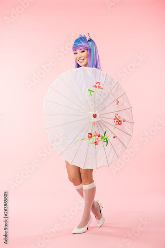 Full length view of smiling asian anime girl holding paper umbrella on pink