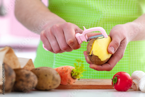 Housewife in apron peeling ripe potato with a peeler for cooking fresh vegetable dishes at home. Proper healthy eating and clean food