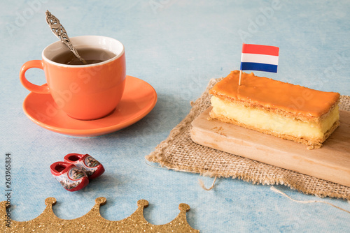 Orange tompouce, traditional Dutch treat with pudding and frosting on national holiday Kings Day (April 27th), in The Netherlands. With cup of coffee, wooden shoes and Dutch flag