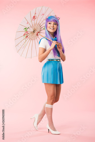 Full length view of smiling asian anime girl holding paper umbrella on pink © LIGHTFIELD STUDIOS