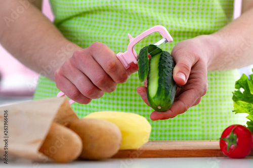 Peeling cucumber with a peeler for cooking fresh dishes and vegetables salads at home. Proper healthy eating and clean food