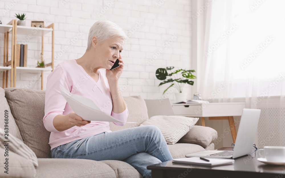 Upset senior woman talking on phone and working at home Upset senior woman talking on phone and working at home