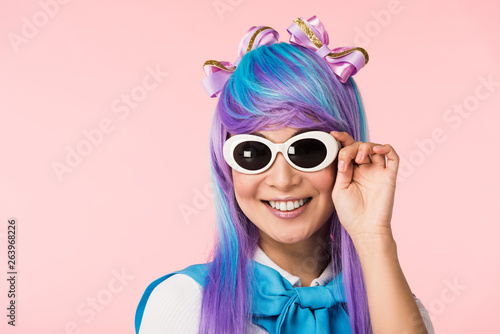 Smiling anime girl in wig and sunglasses isolated on pink