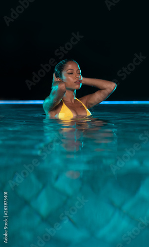 Beautiful woman in yellow bikini relaxing in outdoor swimming pool during night © stryjek