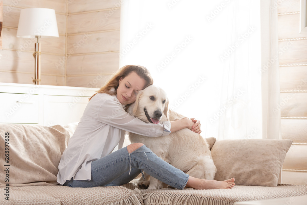 Young pretty woman in casual clothes hugging her beloved big white dog sitting on the sofa in the living room of her cozy country house. Animal communication concept Young pretty woman in casual clothes hugging her beloved big white dog sitting on the sofa in the living room of her cozy country house. Animal communication concept