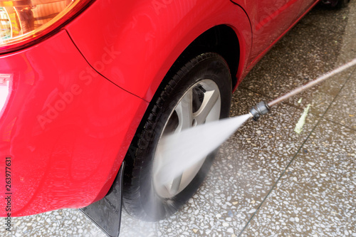 high pressure water jet directed at the wheel of a red car. Car wash image