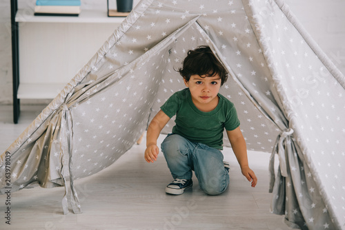 cute kid in jeans sitting in grey wigwam at home photo