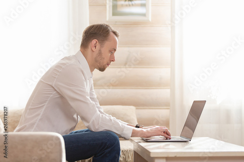 Young male businessman chatting with his colleagues in social networks sitting on the sofa in his designer lounge in the luxury apartment © Rithor